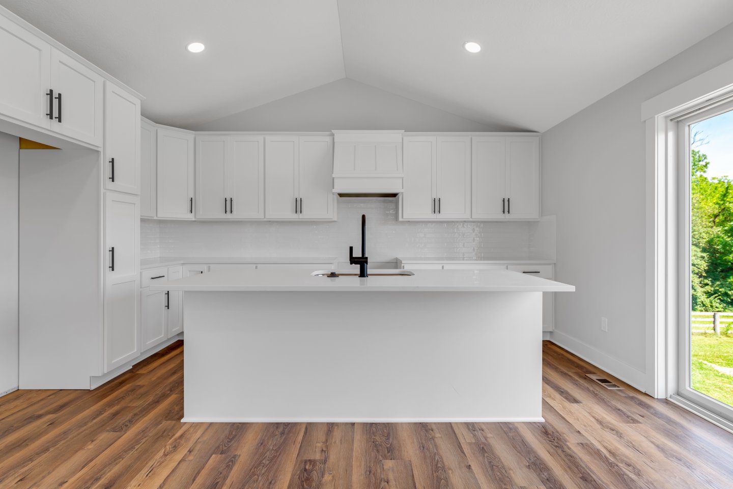 Bright white kitchen with shaker cabinets, large center island, quartz countertops, and stainless steel appliances in a custom ranch home.