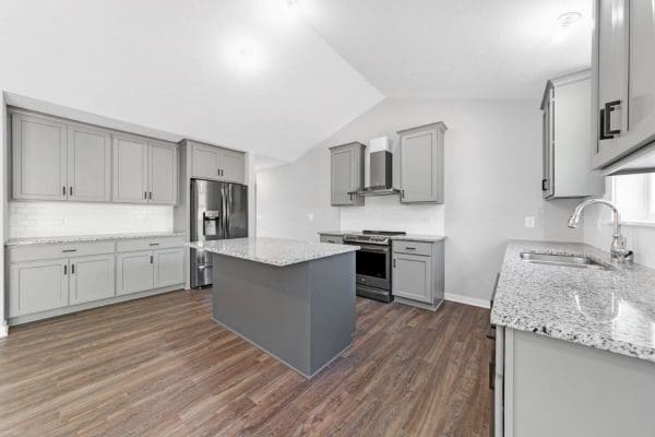 Open-concept kitchen with a gray center island, white shaker cabinets, vaulted ceiling, and luxury vinyl plank flooring.