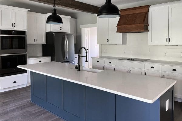 Custom kitchen with blue island, white cabinetry, quartz countertops, black pendant lights, and stainless steel appliances.