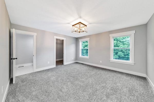 Primary bedroom with carpet flooring, tray ceiling, and large windows overlooking the backyard.