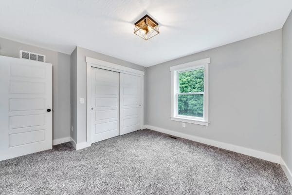 Secondary bedroom with carpet flooring, large window, and double-door closet.