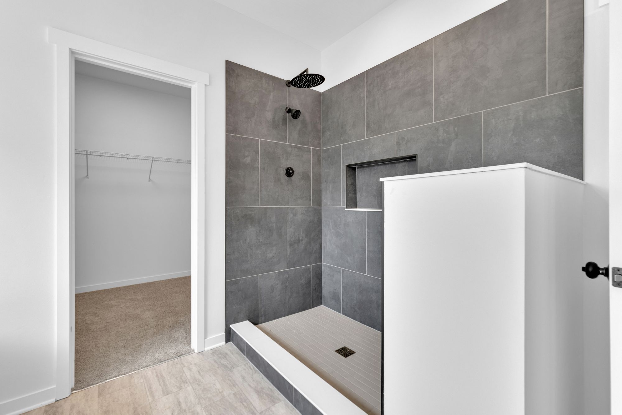 Primary walk-in shower with floor-to-ceiling tile, built-in bench, and frameless glass enclosure.