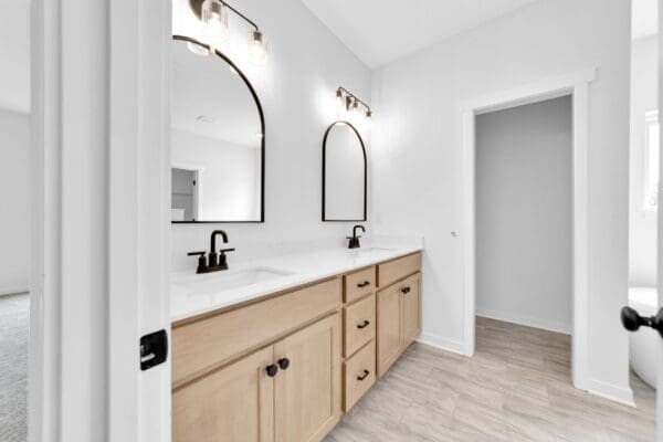 Primary bathroom with a wood vanity, quartz countertop, arched mirrors, and modern black fixtures.
