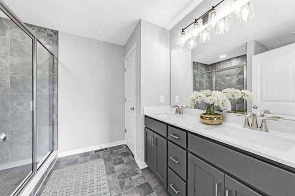 Primary bathroom with a double vanity, dark gray cabinetry, quartz countertops, and framed mirrors.