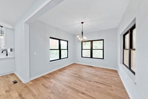 Bright dining room with large black-framed windows, hardwood flooring, and modern pendant lighting.