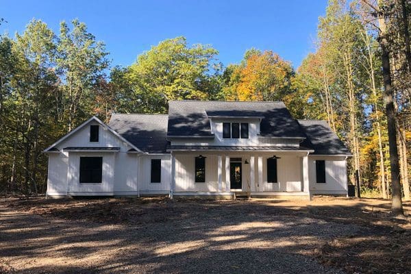 Front elevation of a custom two-story home with covered porch and attached garage surrounded by mature trees.