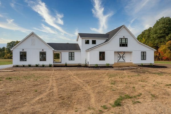 Front exterior of a custom home with white board and batten siding, decorative gables, and a covered front porch.