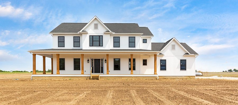 A two-story farmhouse called the Meadowbrook featuring white siding, black windows and roof, and a large wrap around porch.