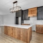 Modern kitchen with island, black cabinetry, natural wood accents, and geometric pendant lighting.